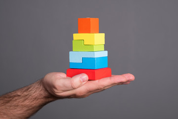 Toy pyramid in a male hand. Hand holds a children's toy on a gray background.