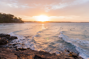 Colourful sunset and sky at the shore. Big and bright sun hiding in the sea. Waves crashing the rocks. Horizontal