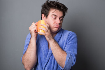 Sleepy man in a bathrobe drinks morning coffee or tea.