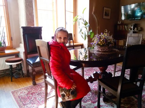 A girl in a red coat and headscarf sits on a chair in a beautiful living room with old durniture.