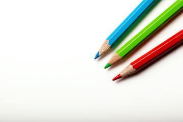 Three colored wooden crayons, diagonally on a white background. Flat lay with copy space.
