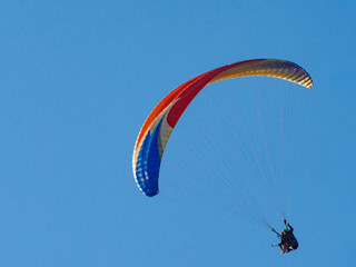 Paraglider flying in blue sky.