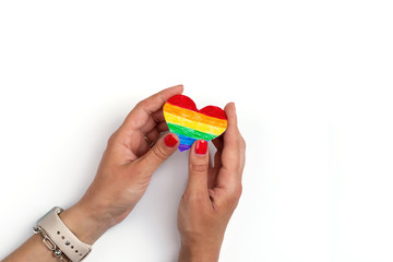 Mockup made with the LGBT pride flag with the heart coloured in LGBTQ pride colours. Concept of the Pride day, Valentine day, freedom, love. Hand holding heart. Flat lay, top view, template, overhead.