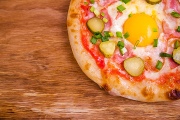 Pizza with ham, egg, pickled cucumber on a wooden background