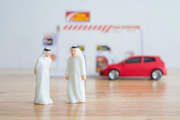 Spending or investment of a country's revenues from petroleum exports industry (Petrodollar). Arab men talking about oil price with gas station and car background. Concept of crude oil price down.
