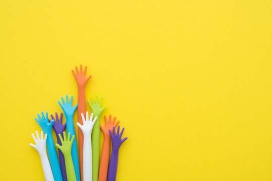 Many colorful hands up on yellow background with copy space. Concept of international human rights, equality and peace. Color hands are symbol of diversity.