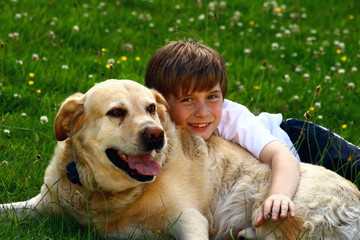 boy hugging dog lying on green grass in garden, at home