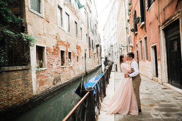 Fototapeta na wymiar Romantic, fairytale, happy newlywed couple hugging and kissing in Venice, Italy
