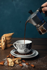 Hand pouring coffee from a coffee pot, homemade Italian cookies cantuccini and almond seeds