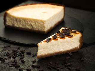 delicious homemade classic New York cheesecake and a slice of watered caramel topping with chocolate chips on a dark background