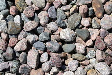Plenty of colorful quite smooth pebble stones by a seashore. Some of the rocks are wet and some dry. Closeup nature photo. Sunny summer day. Calm, relaxing, zen-like photo of a lot of rocks.