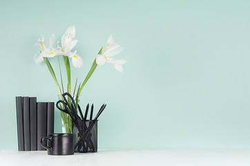 Modern elegant home workplace with black stationery, books, coffee cup, fresh spring white flowers in transparent glass vase green mint menthe interior on white wood table.