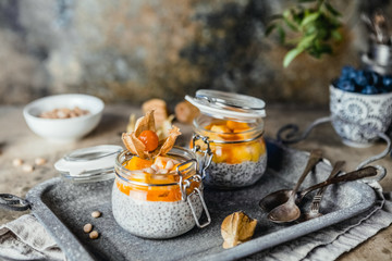  pudding with chia seeds in jars with mango slices and pine nuts on shabby beige background,...