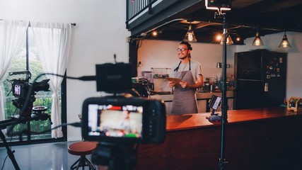 Asian barista man standing in front of the camera and recording vlog video live streaming at bar counter in coffee shop interior background.Sale and promotion online marketing business concept. - 346087264