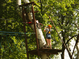 Naklejka na ściany i meble Yaslo, Poland - 8 7 2019:A young girl climbs the trees in gear in a park for rock climbing. Scandinavian attraction for sports events. Rope insurance and means of protection. Safety at altitude