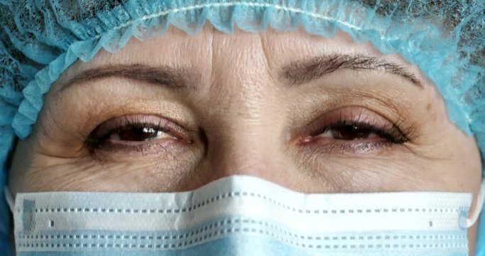 Close-up. Caucasian doctor woman in medical mask smiles and nods her head approvingly. Kind eyes of the doctor in a protective mask. COVID-19