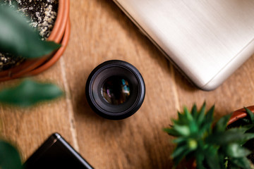flat lay. laptop, cell phone, lens, flower stand on a wooden background. top view
