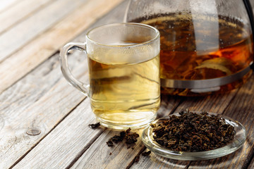 Hot green tea in glass mug. Dried tea leaves and hot drink on a wooden table.