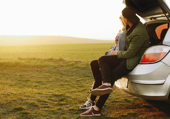
Couple sitting in the trunk of the car and looking at the sunset. Travel, trip, tourism concept. - obrazy, fototapety, plakaty