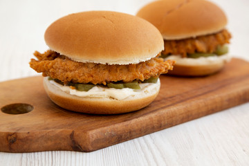 Homemade Burgers with fried chicken strips on a rustic wooden board on a white wooden background, low angle view. Close-up.