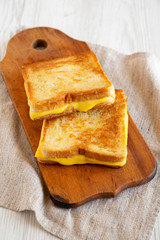 Homemade Grilled Cheese Sandwich on a rustic wooden board on a white wooden background, side view.