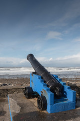 Fototapeta na wymiar Old cast metal iron cannon by the ocean, Black gun barrel blue carriage. Strandhill beach, county Sligo, Ireland, Cloudy sly over Atlantic ocean. Nobody.