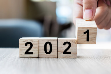 Businessman hand holding wooden cube with block 2021 word on table background. Resolution,...