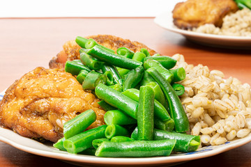 green asparagus beans on a plate with golden chicken thighs and pearl barley. healthy diet food.