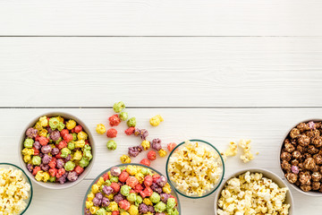 Obraz na płótnie Canvas Colored popcorn in bowl on white wooden background top view copy space