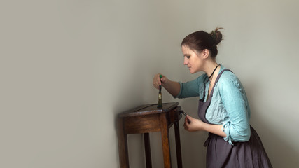 woman in work apron paints table with brush, reuse