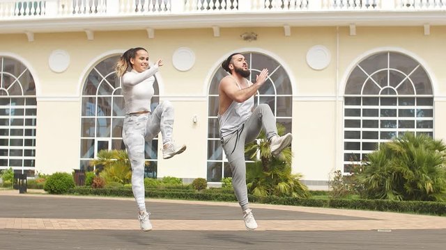 Cheerful caucasian couple training outdoors doing crossfit exercise at beautiful building background.