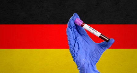 medicine, healthcare and virus concept - close up of hand in protective medical glove holding beaker with coronavirus blood test over flag of germany