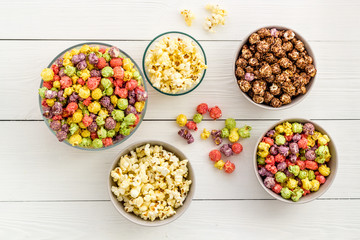 Colored popcorn in bowl on white wooden background top view