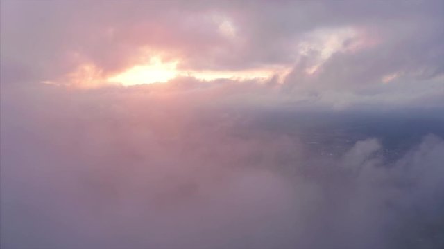 Aerial view of the rural area and clouds running in the sky at sunset. Camera ascends throught the cloud and reveals high altitude view