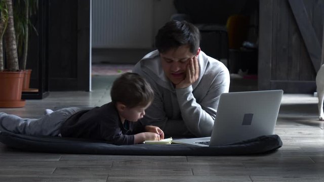 dad is try to work with computer and play with his son at home during the quarantine