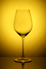 The crystal glass stands on the reflecting surface on a yellow background. studio photo. product. Beautiful shadow from wine glass. macro photo
