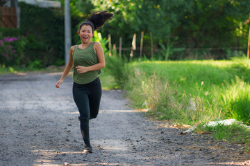 outdoors running workout - young happy and dedicated Asian Korean woman jogging at beautiful city park or countryside trail on sunset enjoying fitness in healthy lifestyle