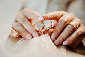 two golden rings in the hands of the bride that lie on a wedding white veil with a blurred...