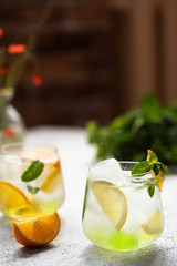 Two glasses with lemonade with oranges, lemons and mint. Buch of peppermint and vase with poppies on a table. Sunny day and refreshing beverage