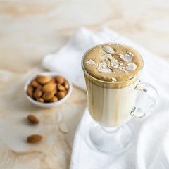 A popular Korean drink during self-isolation is Dalgona coffee. A delicious modern cold beverage with an almond nut snack and textile napkin is on the marble table.