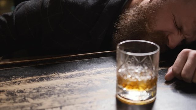 drunk man fell asleep at bar with glass of whiskey, Bourbon, Rum, feeling headache, Caucasian with beard and mustache, looks bad and upset, mumbles, close up, 4k