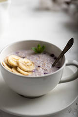 Close-up view of cup with oatmeal porridge with bananas and mint leaves. Healthy breakfast concept