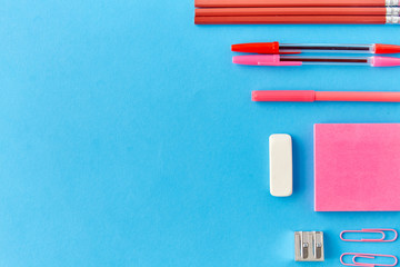 office supplies, stationery and object concept - pink sticky notes, clips, pens with pencils and eraser on blue background