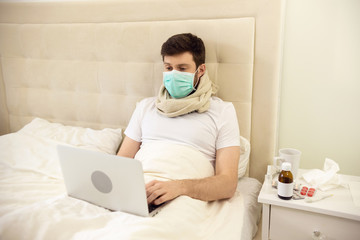 Sick Man Working in Bed Wearing Medical Mask. Man Working at Home. Man Using Laptop in Bed. Man Ill at Home. Quarantine, Home Work, Medical Care.