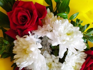 Beautiful bouquets of white chrysanthemums and red roses with green leaves in yellow packaging