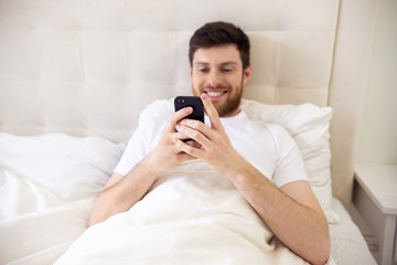 Man Chatting on Phone in Bed. Morning at Home. Smilling Man Using Phone in Bed. Quarantine, Home Work, Medical Care.