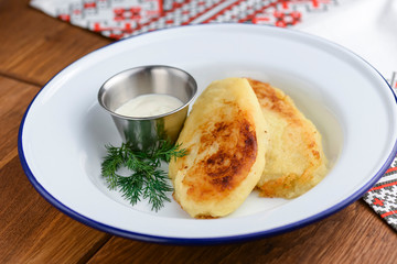 Closeup of freshly fried potato pancakes with sour cream in white plate over rustic wooden table background.