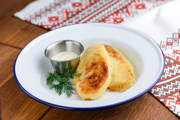 Closeup of freshly fried potato pancakes with sour cream in white plate over rustic wooden table background.