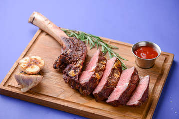 Sliced grilled Medium rare barbecue Steak on bone with spices served on a rustic wooden board over blue background.