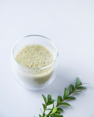 fresh matcha tea in a clear glass with flowers on blue background. Trendy diet drink